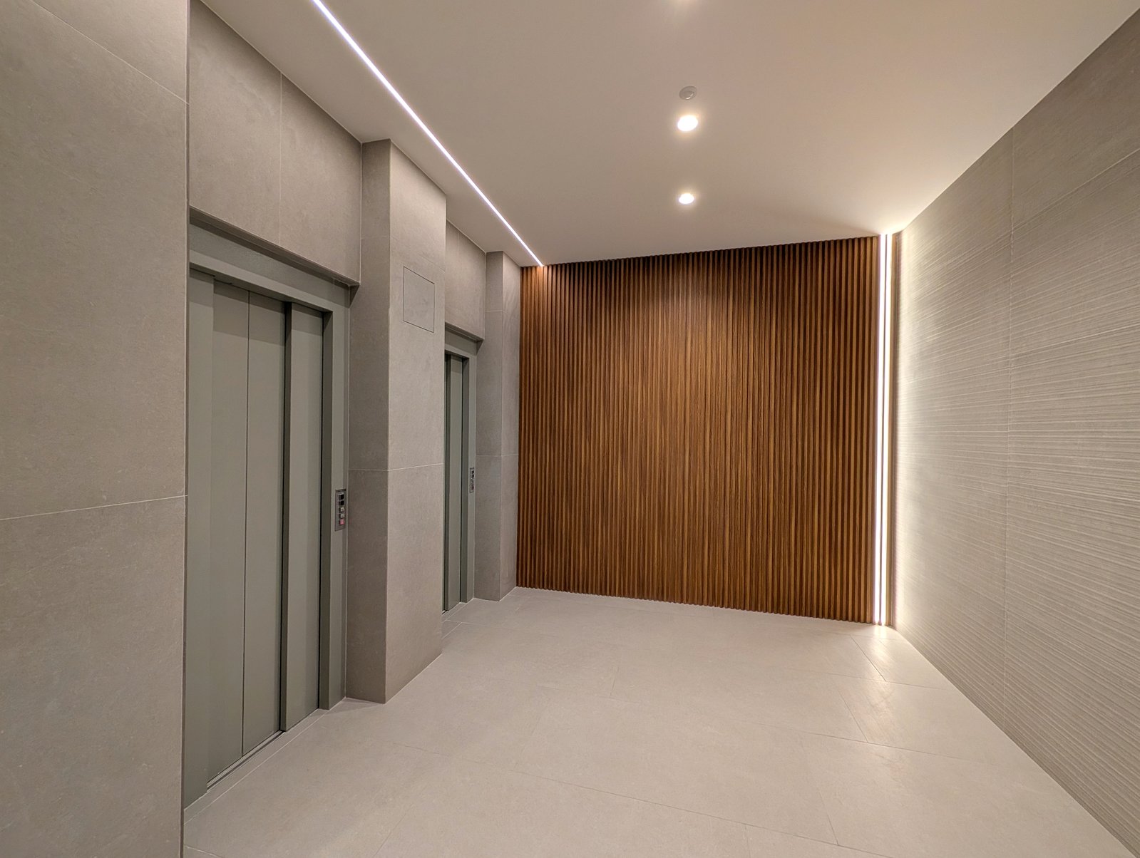 Zona de ascensores rehabilitada con panel vertical de lamas de madera e iluminación LED perimetral - Madrid Grupo Illescas
